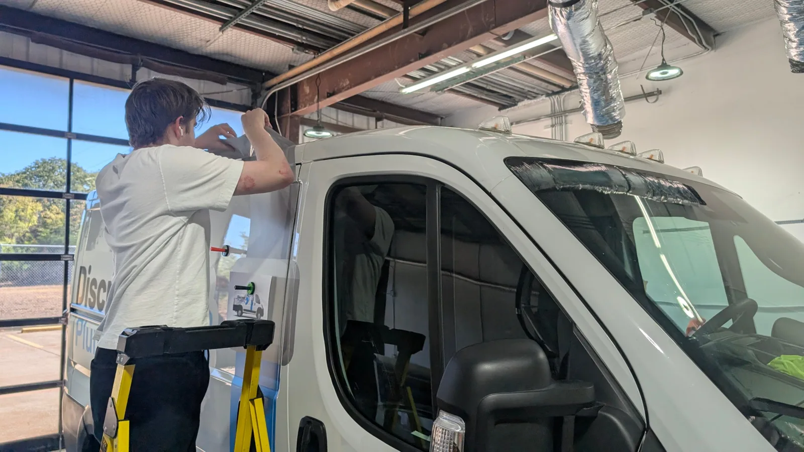 Installer trimming the wrap at the cab edge of the Discreet Plumbing van