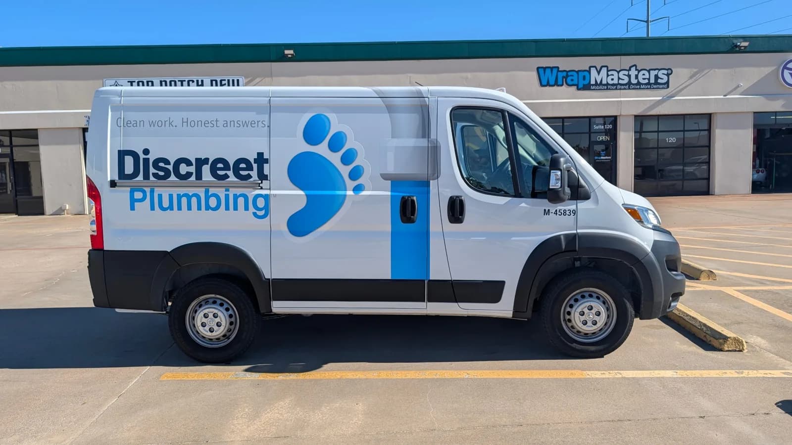 Discreet Plumbing Ram ProMaster van with a partial wrap: the name, a blue footprint mark, and the line Clean work. Honest answers., parked outside WrapMasters in Denton