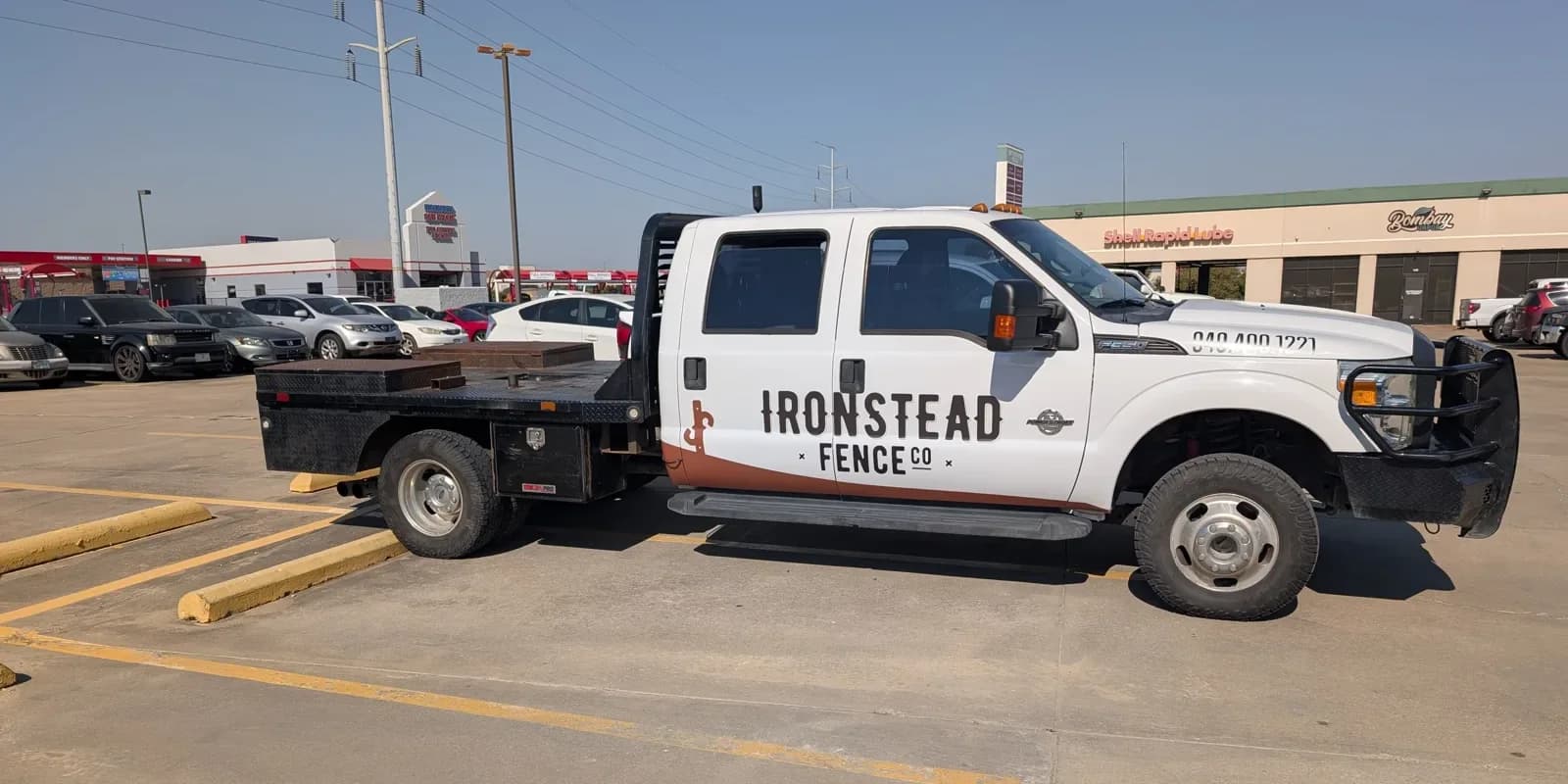 The same F-350 flatbed after the wrap: Ironstead Fence Co. across the doors with the brand mark and a brown stripe