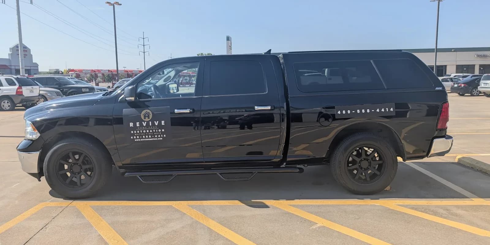 The Revive Home Pros pickup before the wrap: a black truck with a small door decal and a phone number on the bed cap