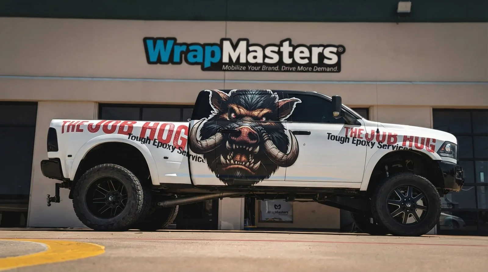 The Job Hog lifted pickup wrapped in white with a snarling hog and The Job Hog name on the side